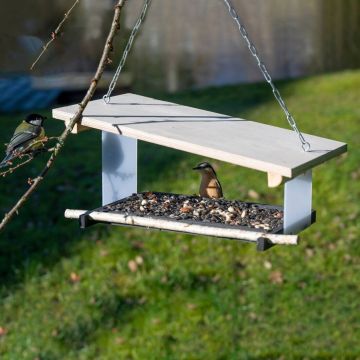Hängendes Vogelhaus aus Holz mit Metallketten, gefüllt mit Vogelfutter, zwei kleine Vögel sitzen am Futterhaus. Im Hintergrund Rasen und Bäume.
