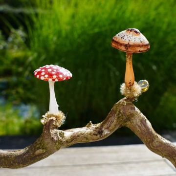 Zwei dekorative Pilzfiguren, ein Fliegenpilz mit rotem Hut und weißen Punkten sowie ein brauner Pilz, stehen auf einer gekrümmten Astnachbildung vor grünem Hintergrund.