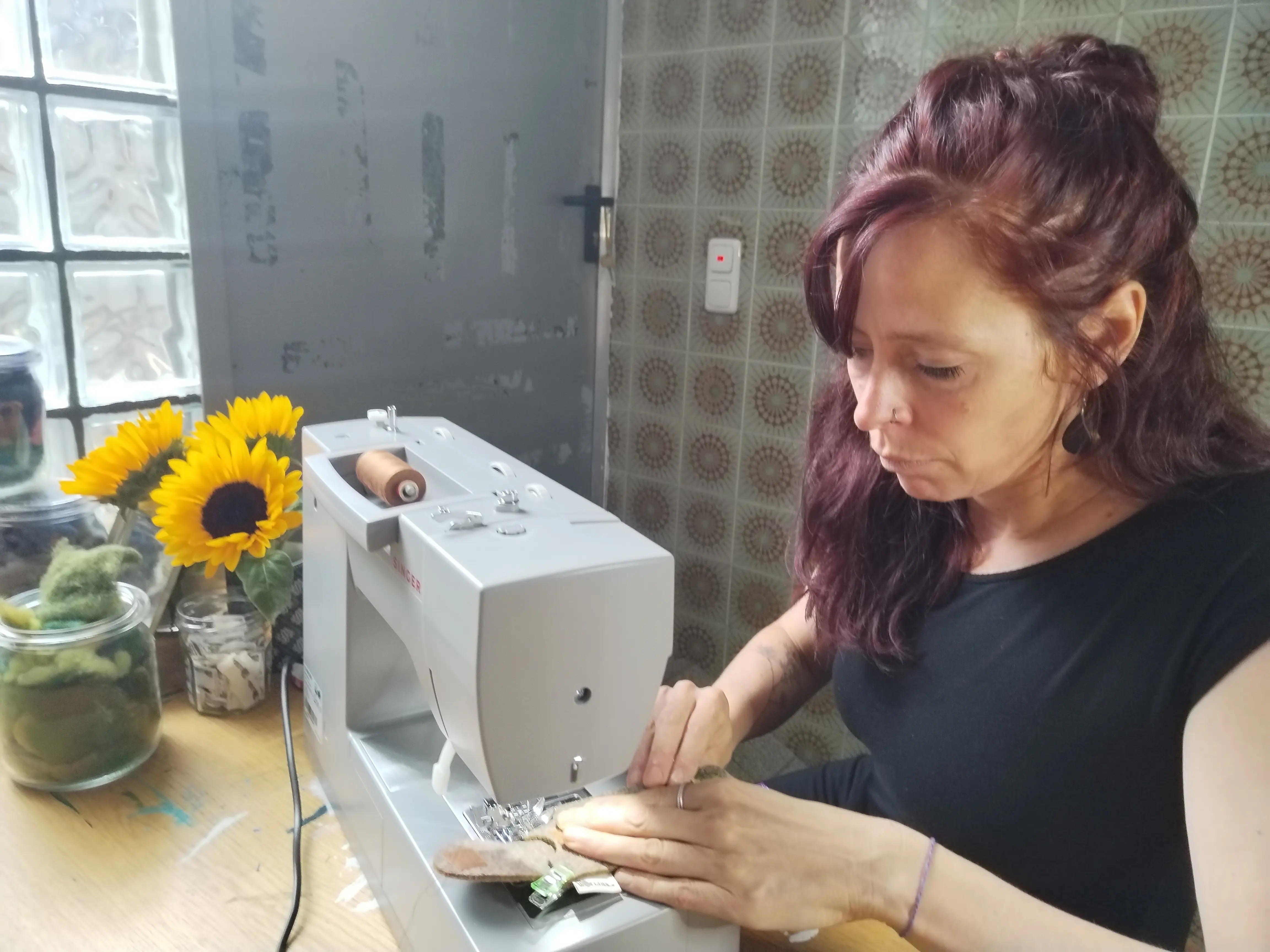 Frau sitzt an einem Tisch und näht mit einer Nähmaschine das Filzetui.