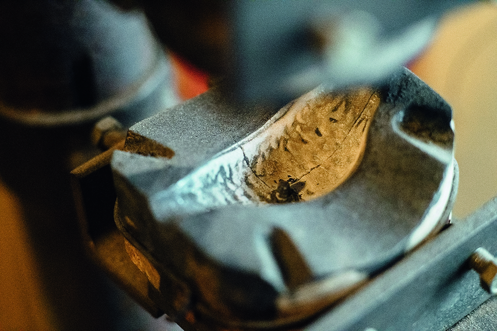 Ein Metallteil wird auf einer Industrieeinrichtung bearbeitet, möglicherweise im Rahmen eines Herstellungsprozesses. Die Nahaufnahme zeigt Spuren der Bearbeitung auf der Oberfläche.