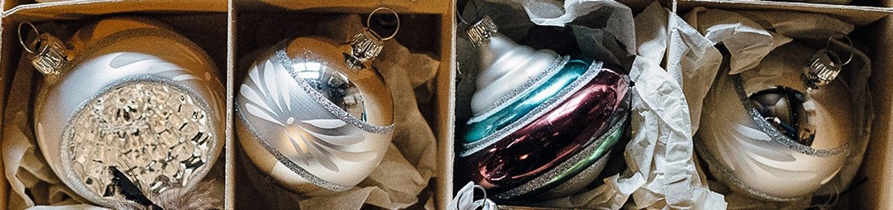 Vier Weihnachtskugeln in Kartons mit Papier ausgelegt; zwei sind silbern mit Mustern, eine glänzt in Silber und Blau, die letzte ist mehrfarbig in Silber, Blau und Rot.