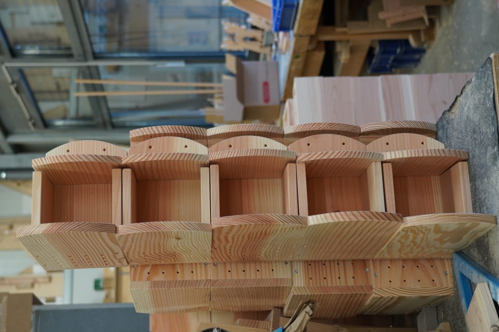 Gestapelter Holzregal-Prototyp auf einem Tisch in einer Werkstatt mit Werkzeugen und Materialien im Hintergrund.