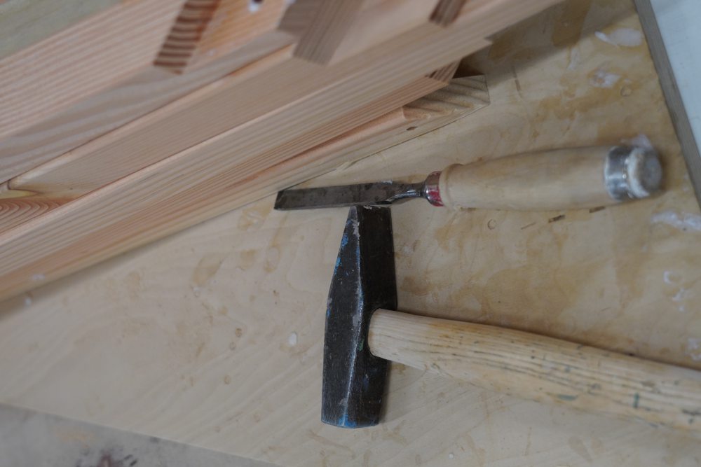 Hammer und Stechbeitel liegen neben einer gefrästen Holzverbindung auf einer Werkbank.
