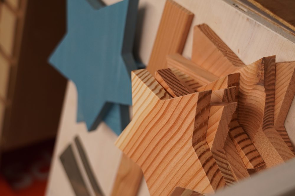 Gestapelte Holzsterne in Naturholz und blau, auf einem Tisch liegend, umgeben von weiteren Holzstücken.