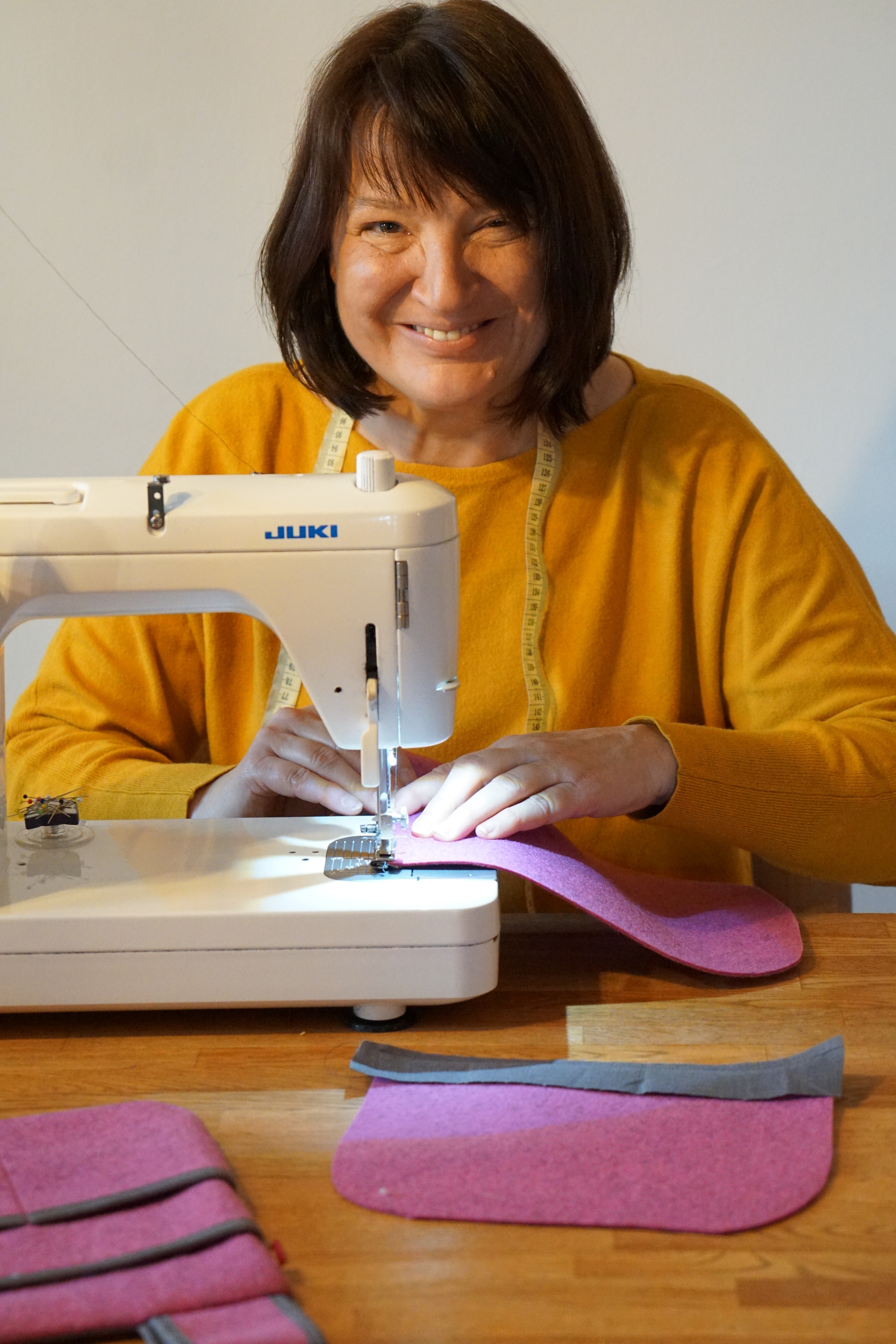 Eine Frau sitzt hinter einer Nähmaschine und lächelt in die Kamera.