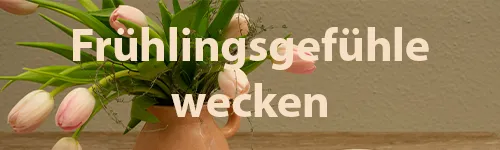 Ein keramischer Krug mit rosa Tulpen und grünen Blättern vor einer beigefarbenen Wand. Der Text "Frühlingsgefühle wecken" überlagert das Bild mittig in großer, weißer Schrift.