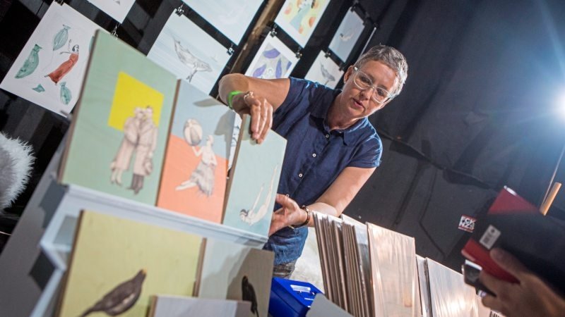 Illustratorin, die hinter den handgezeichneten Bildern aus Travertin-Natursteinfliesen steht, sie berührt ein Bild , es ist eine Messe artige Atmosphäre.