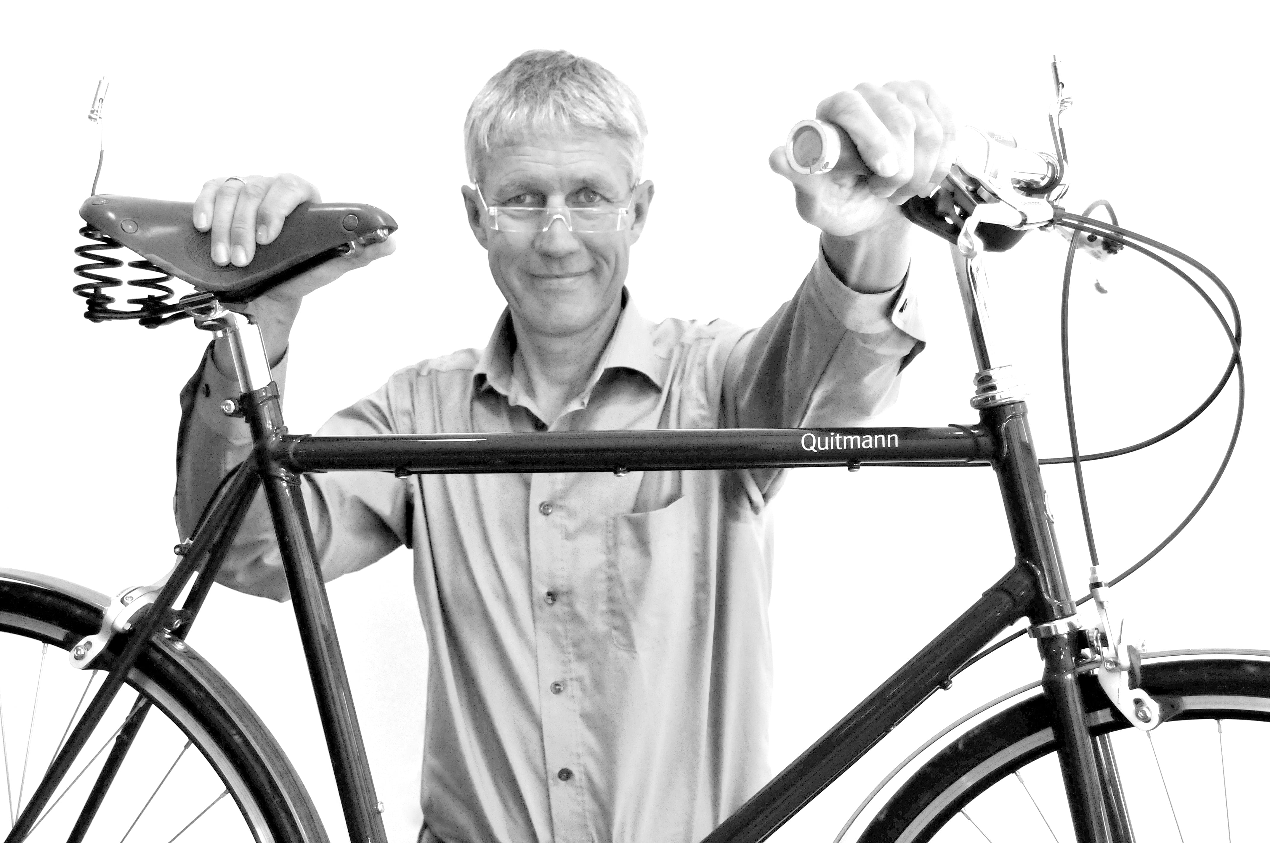 Eine Person in einem hellen Hemd hält ein Fahrrad am Sattel und Lenker. Das Fahrrad ist im Querformat vor der Person positioniert. Der Hintergrund ist weiß. 