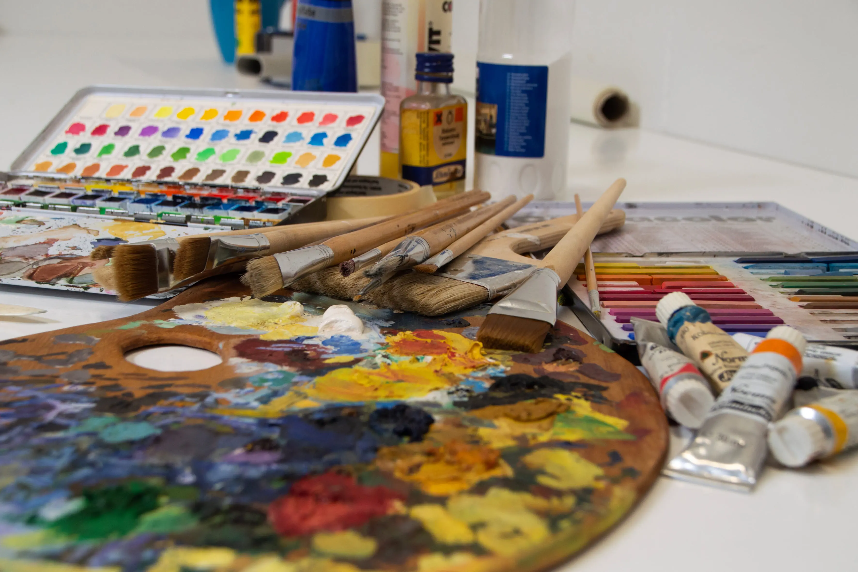 Eine Farbpallette, mit verschiedenen Farben liegt auf dem Tisch, darüber mehrere Pinsel und und Stifte.